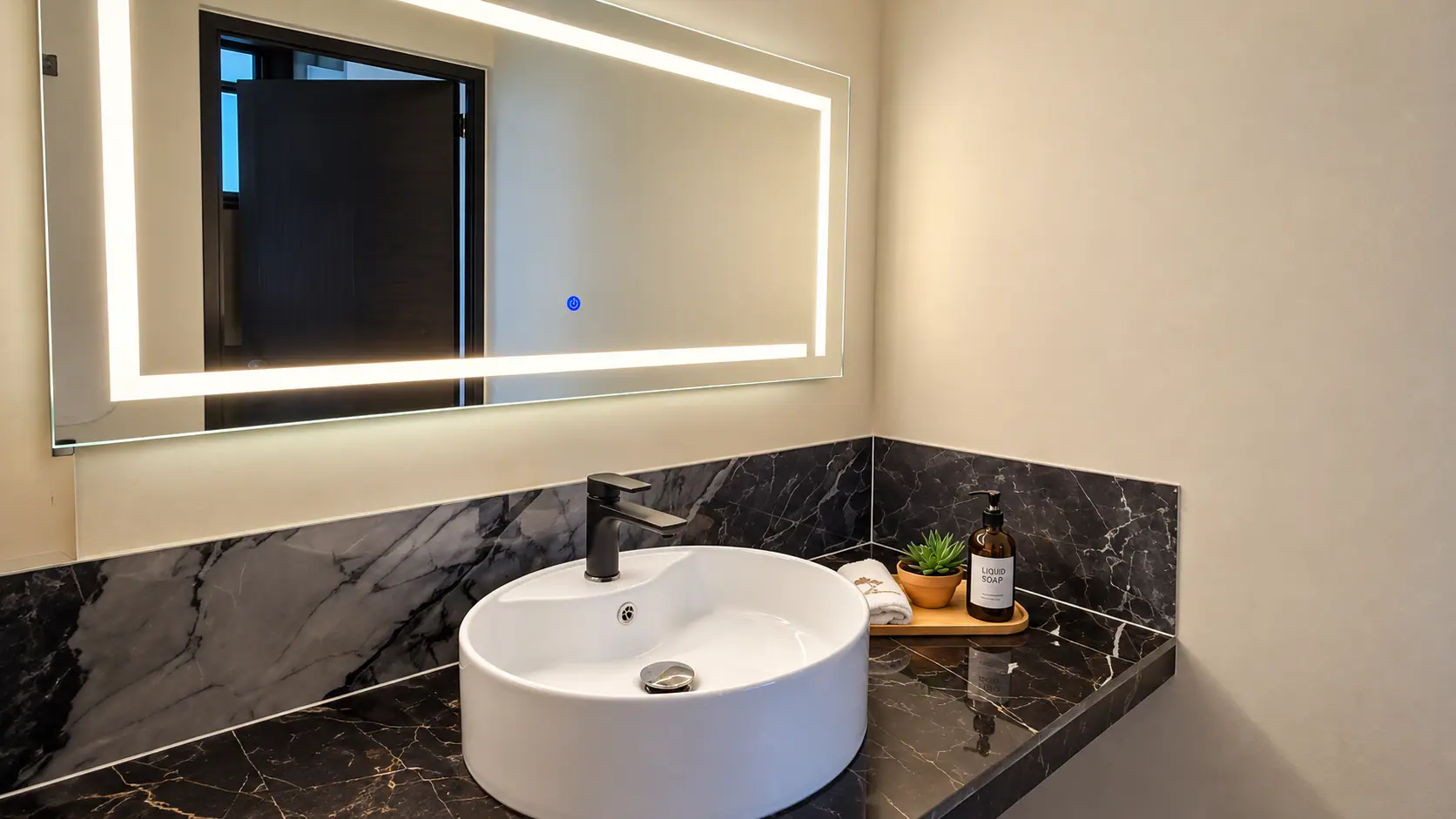Lavabo sobre encimera de mármol negro con espejo iluminado en Coco Beach